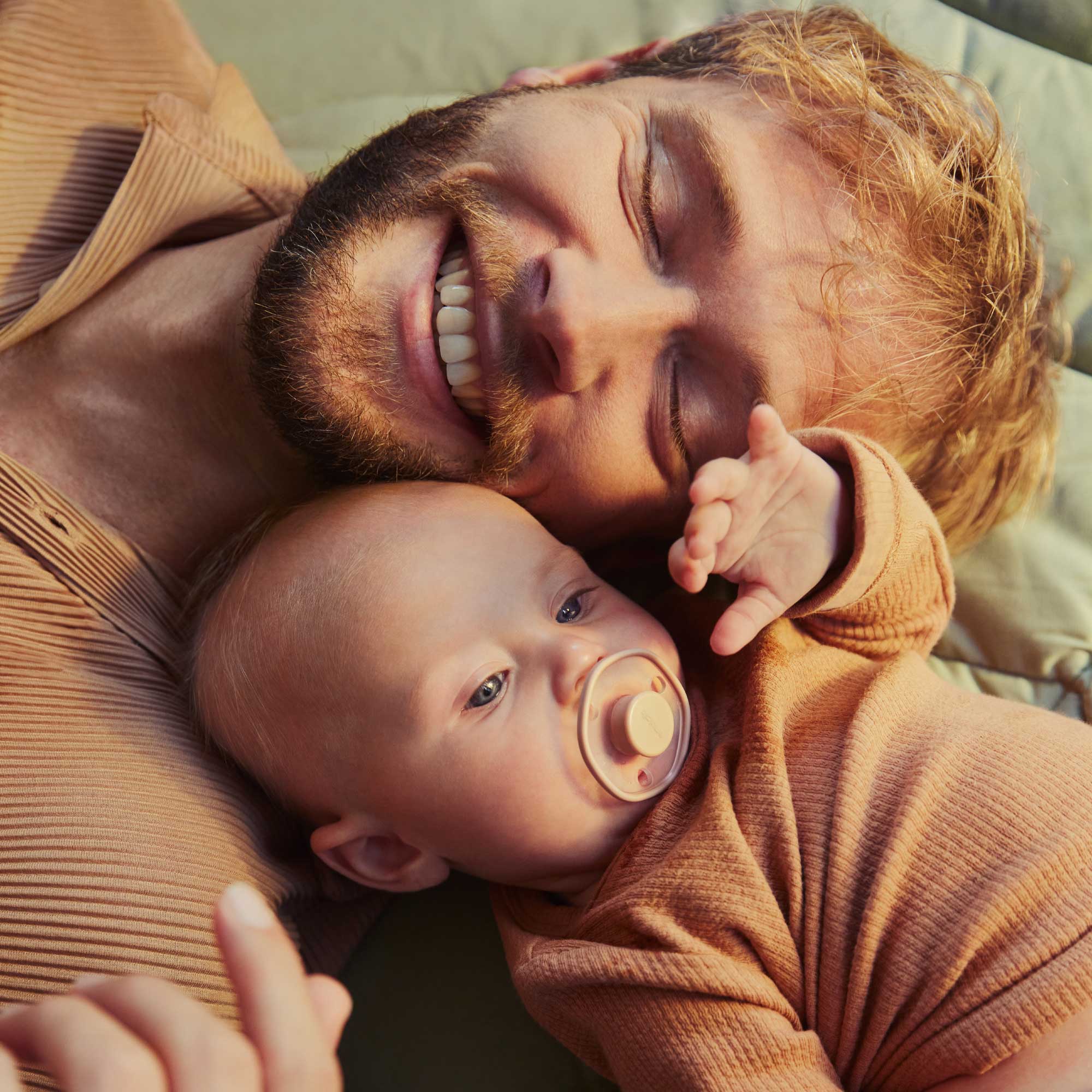 Smilling father and laying baby with pacifier in his mouth